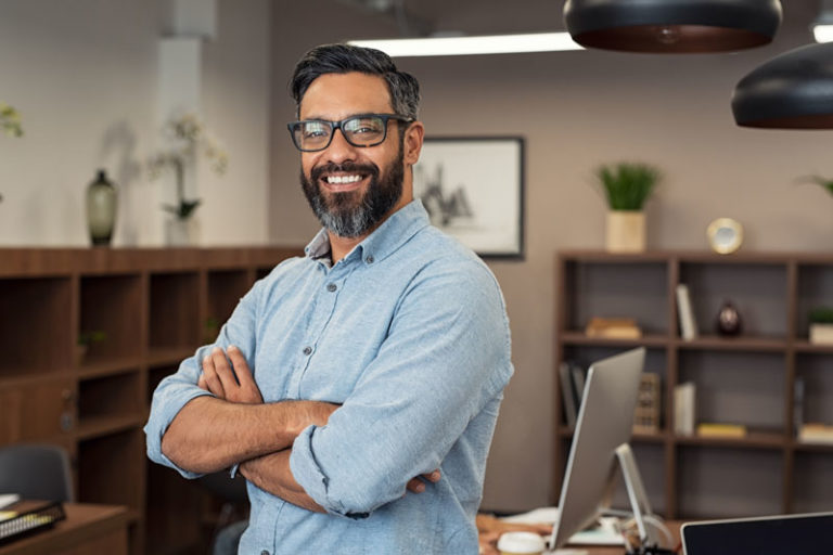 Smiling man wearing glasses with arms folded standing in office