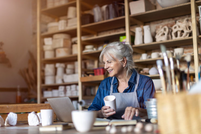 Smiling old woman in pottery room looking at a laptop