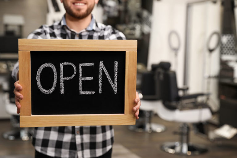 Close-up of man holding chalk board sign with "open" written on it